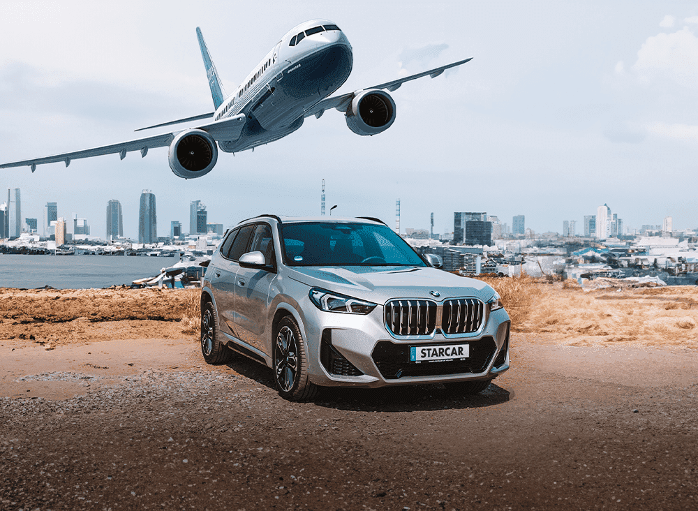 Silberner BMW X1 Mietwagen mit startendem Flugzeug im Hintergrund.