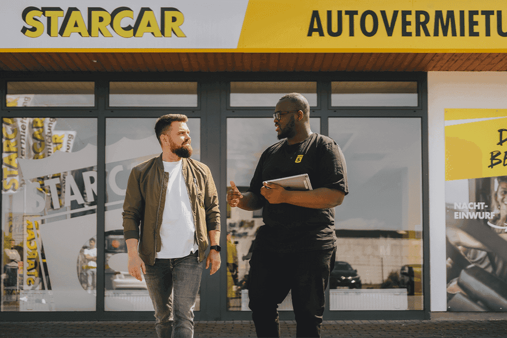 Zwei Männer unterhalten sich vor einem STARCAR-Station.