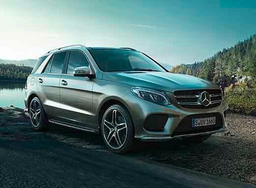 Silberner Mercedes Benz GLE350, geparkt auf einer Schotterstraße in der Nähe eines Sees.
