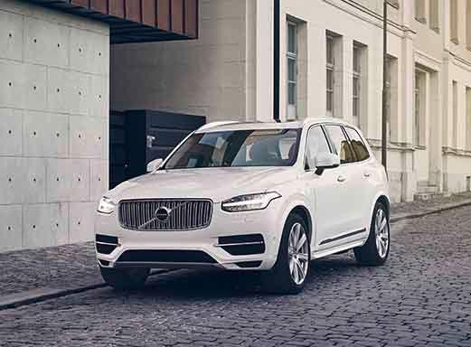 White Volvo XC90 parked on a cobblestone street near a building.