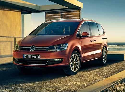 Red VW Sharan minibus parked near a building and the sea.