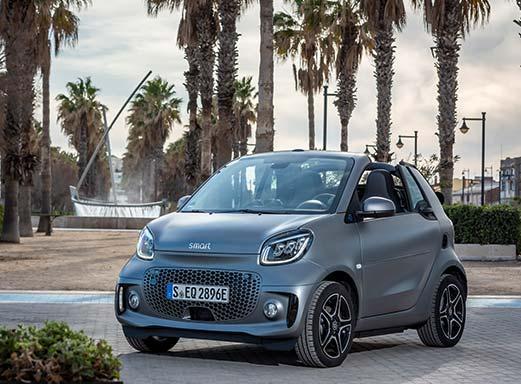 Graues Smart Fortwo Cabrio auf einer Straße mit Palmen im Hintergrund.