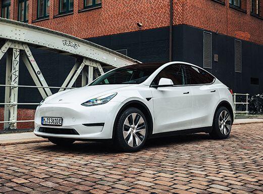 Weißes Tesla Model Y Elektroauto auf gepflasterter Straße.